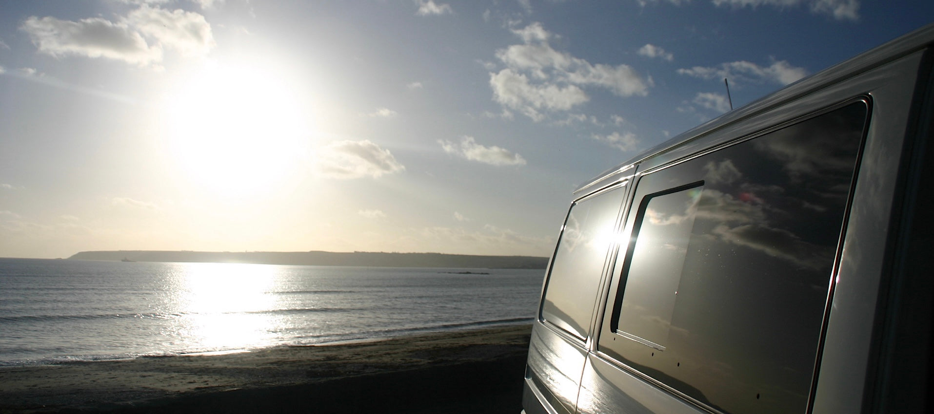 Van parked on a beach with ocean and sunset in the background