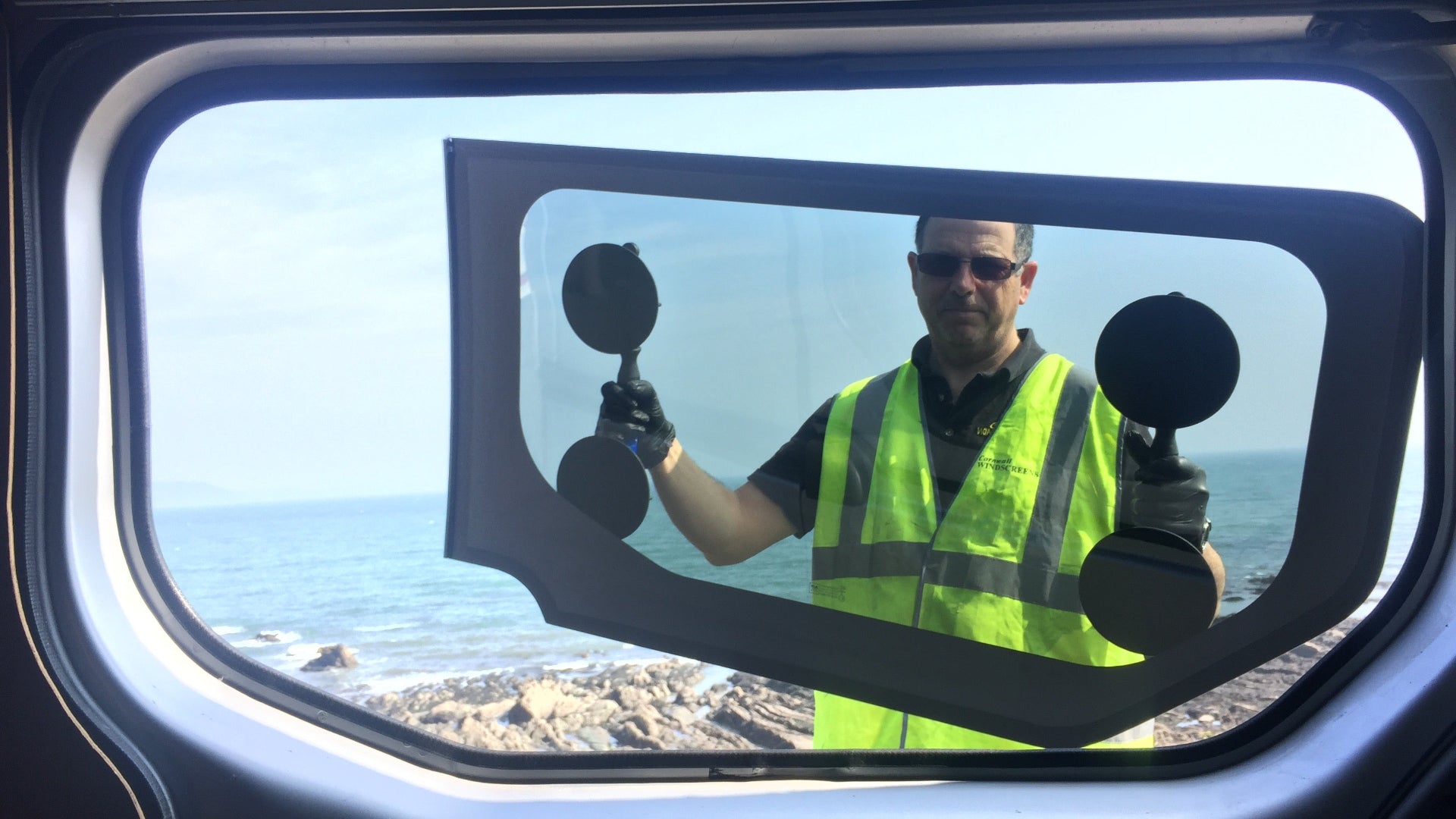 Person in a high-visibility vest holding a large van window with a scenic view